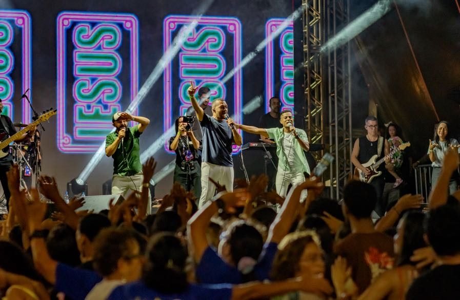 Banda no palco do Luau com Cristo diante do público, com painéis luminosos escritos Jesus